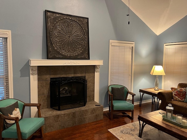 living area featuring vaulted ceiling, wood finished floors, a tiled fireplace, and baseboards