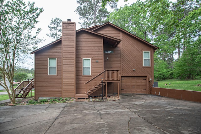 back of property with concrete driveway, an attached garage, a chimney, and stairs