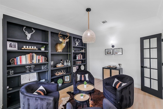 living area featuring visible vents, crown molding, wood finished floors, baseboards, and built in shelves