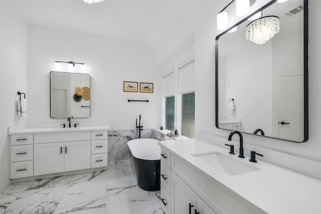 bathroom featuring marble finish floor, a freestanding tub, two vanities, a sink, and vaulted ceiling