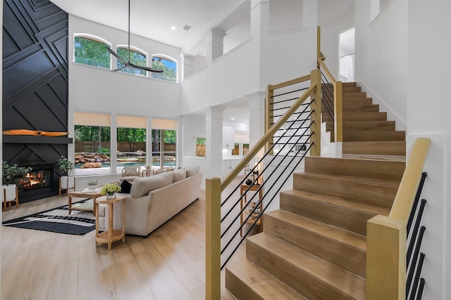 staircase featuring a high ceiling, visible vents, a large fireplace, and wood finished floors