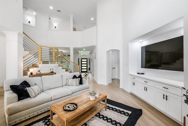 living room featuring stairs, a towering ceiling, baseboards, arched walkways, and light wood finished floors