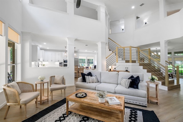 living room with visible vents, decorative columns, a towering ceiling, stairs, and light wood finished floors