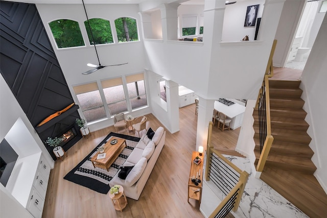 living room featuring a towering ceiling, ceiling fan, stairs, and a warm lit fireplace