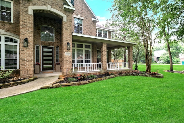 view of exterior entry featuring covered porch, a yard, and brick siding