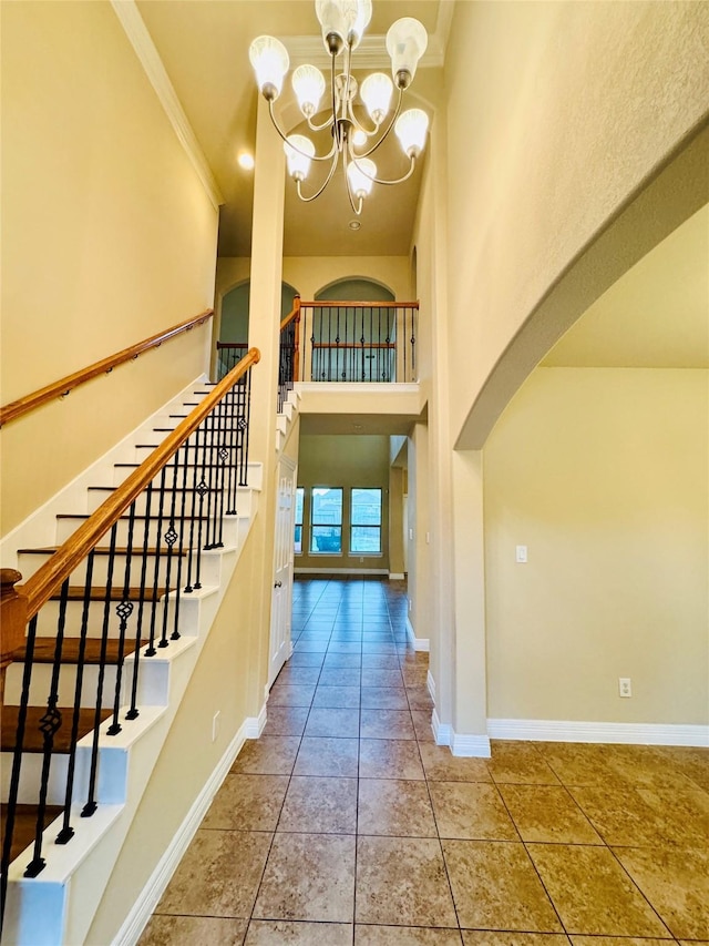 tiled foyer entrance with a high ceiling, arched walkways, an inviting chandelier, baseboards, and ornamental molding