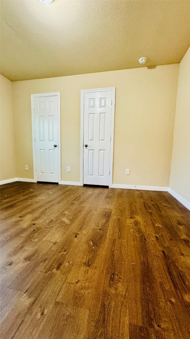 spare room with wood finished floors, a textured ceiling, and baseboards