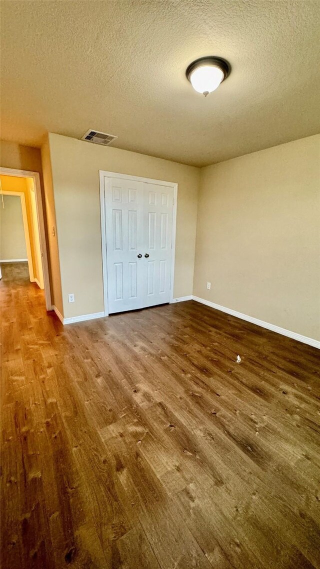 unfurnished bedroom featuring baseboards, wood finished floors, visible vents, and a textured ceiling