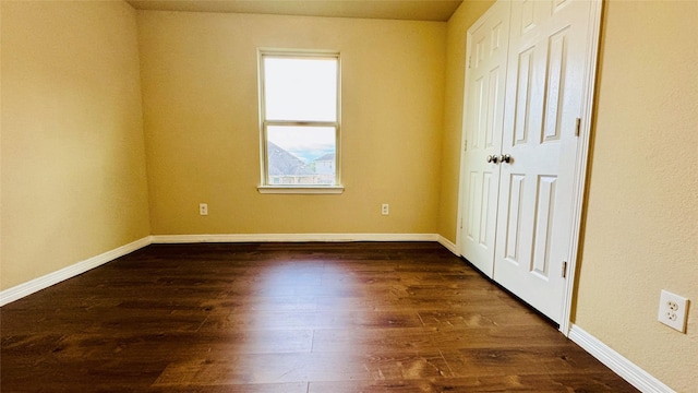unfurnished bedroom with baseboards and dark wood-type flooring