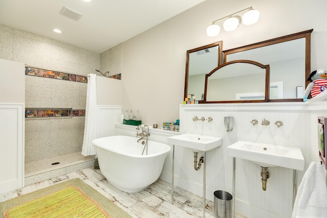 bathroom featuring a wainscoted wall, a freestanding bath, visible vents, a sink, and tiled shower