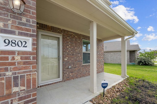 doorway to property featuring brick siding, a yard, and covered porch