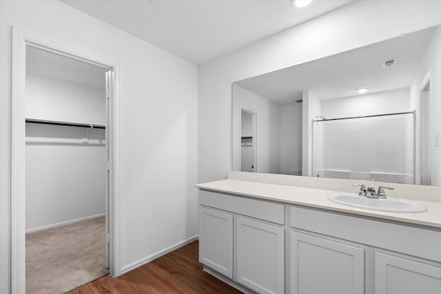 full bathroom featuring wood finished floors, a spacious closet, vanity, a shower, and visible vents