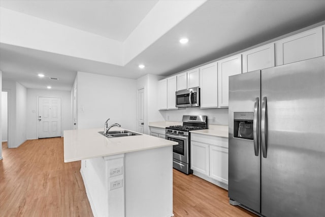 kitchen with white cabinets, an island with sink, a sink, light wood-type flooring, and appliances with stainless steel finishes