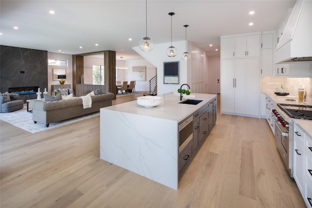 2239 Colquitt St, Houston, TX 77098 - kitchen featuring a sink, light stone counters, white cabinets, extractor fan, and light wood-style flooring