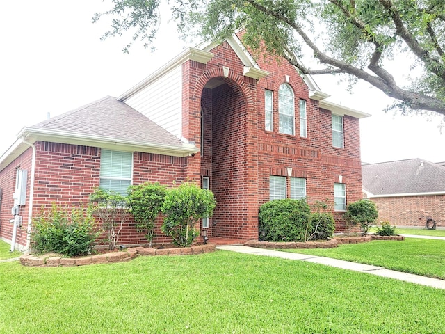 traditional-style house featuring a shingled roof, brick siding, and a front lawn