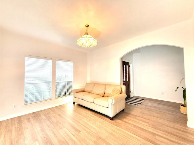 living area with a chandelier, arched walkways, baseboards, and light wood-style floors