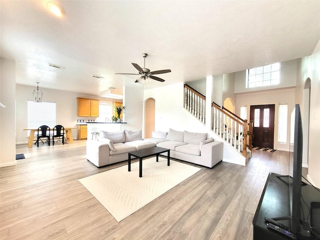living room with light wood finished floors, ceiling fan, visible vents, arched walkways, and stairway