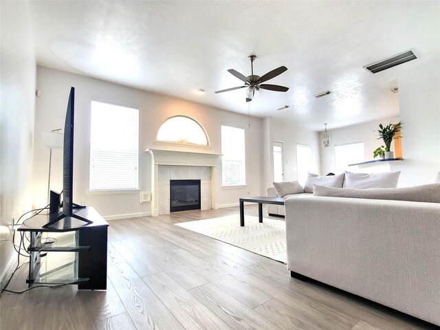 living area with a tile fireplace, wood finished floors, visible vents, baseboards, and ceiling fan
