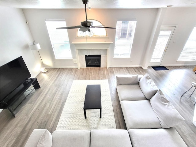 living area featuring wood finished floors, baseboards, a fireplace, and a ceiling fan