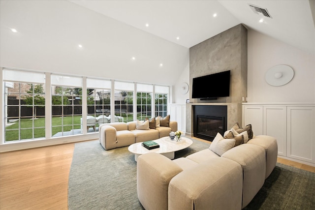 living room with high vaulted ceiling, a glass covered fireplace, wood finished floors, and visible vents