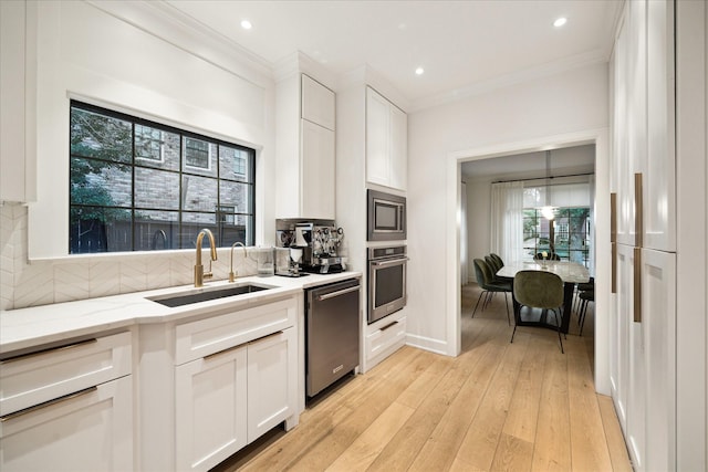 kitchen featuring stainless steel appliances, a sink, crown molding, tasteful backsplash, and white cabinetry