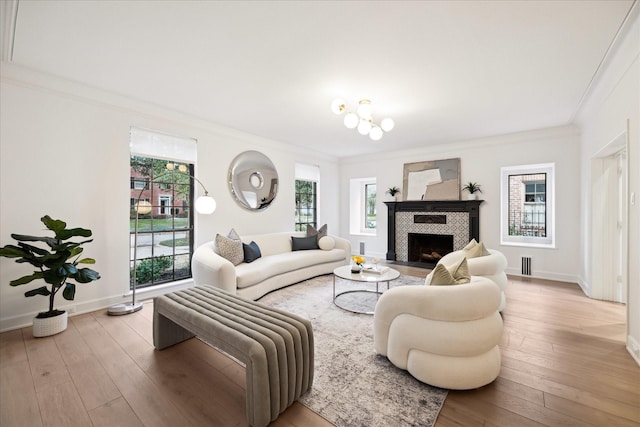 living area featuring wood-type flooring, baseboards, ornamental molding, and a tiled fireplace