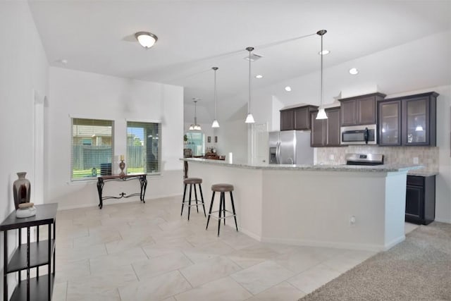 kitchen featuring stainless steel appliances, a large island with sink, dark brown cabinetry, backsplash, and a breakfast bar area