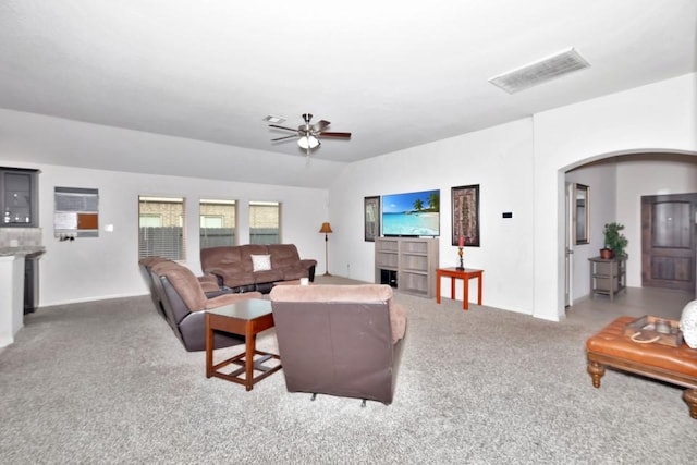 carpeted living area featuring vaulted ceiling, visible vents, arched walkways, baseboards, and ceiling fan
