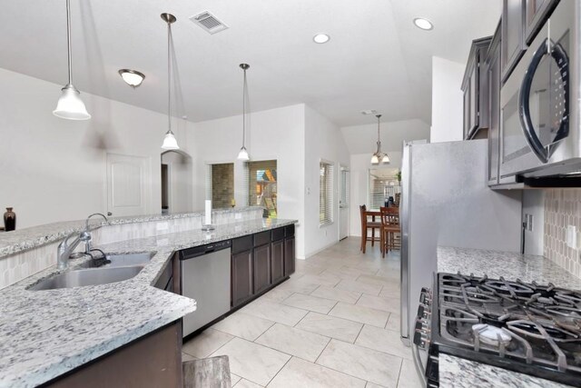 kitchen with a sink, hanging light fixtures, appliances with stainless steel finishes, light stone countertops, and visible vents