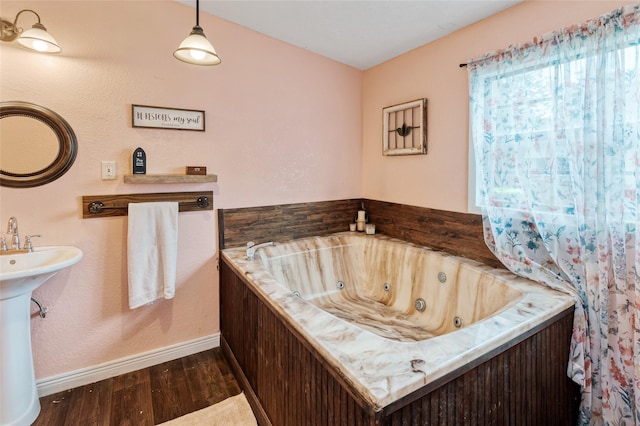 bathroom featuring wood finished floors, baseboards, a sink, and a tub with jets