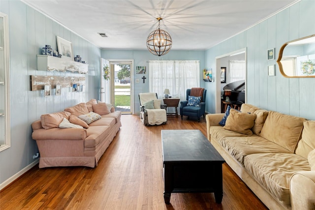 living room featuring an inviting chandelier, ornamental molding, wood finished floors, and visible vents