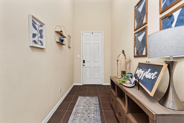 doorway featuring dark tile patterned floors, a towering ceiling, and baseboards