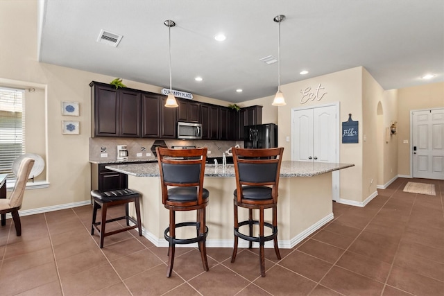 kitchen featuring backsplash, visible vents, stainless steel microwave, freestanding refrigerator, and dark tile patterned flooring