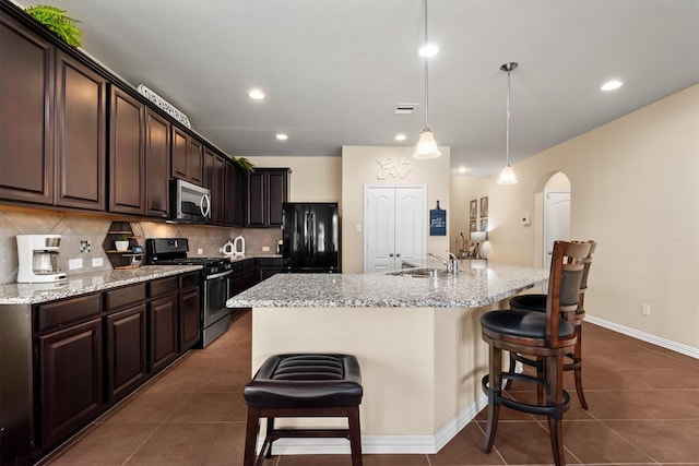 kitchen featuring a kitchen breakfast bar, stainless steel appliances, a sink, arched walkways, and dark brown cabinetry