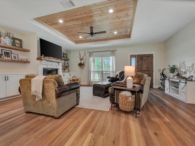 living room with a tray ceiling, visible vents, light wood-type flooring, a lit fireplace, and ceiling fan