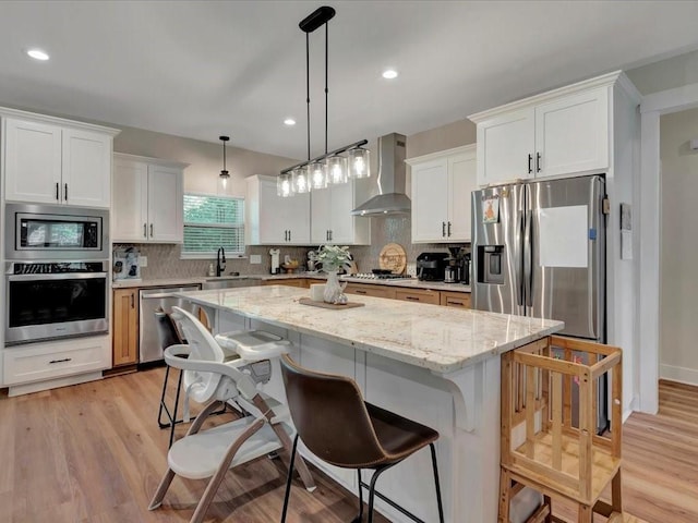 kitchen with decorative backsplash, a kitchen island, appliances with stainless steel finishes, and wall chimney range hood