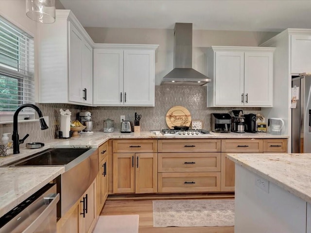 kitchen featuring light stone counters, wall chimney range hood, decorative backsplash, light wood-style flooring, and appliances with stainless steel finishes