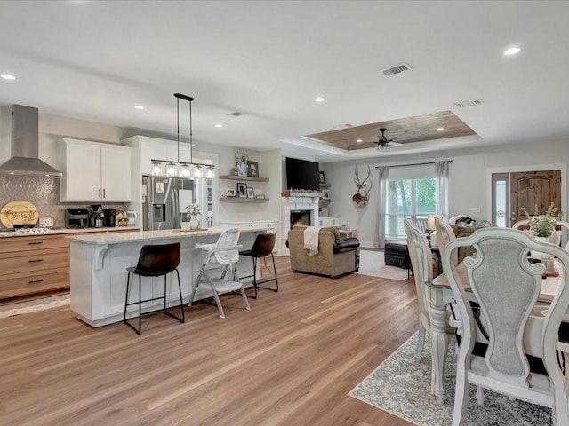 dining area featuring a tray ceiling, light wood-style flooring, visible vents, and ceiling fan