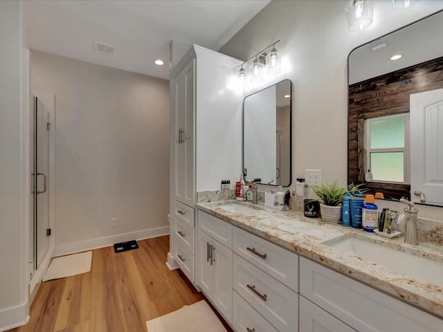 full bathroom featuring a shower stall, wood finished floors, double vanity, and a sink