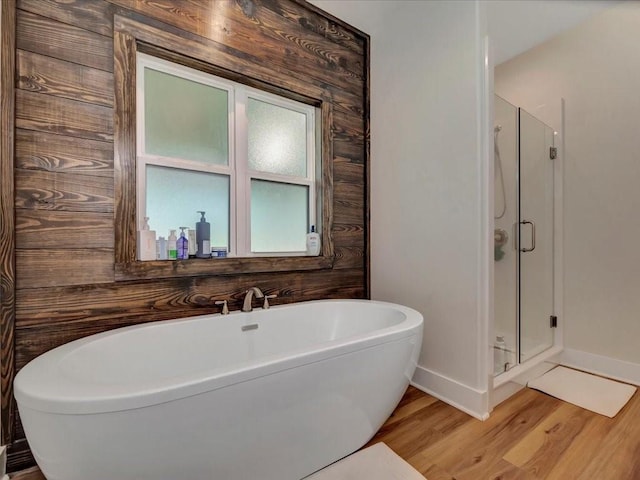 bathroom with a shower stall, baseboards, a soaking tub, and wood finished floors