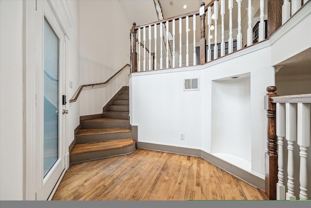 staircase featuring a towering ceiling, wood finished floors, and visible vents