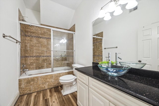 bathroom featuring wood finished floors, vanity, tiled shower / bath combo, toilet, and visible vents