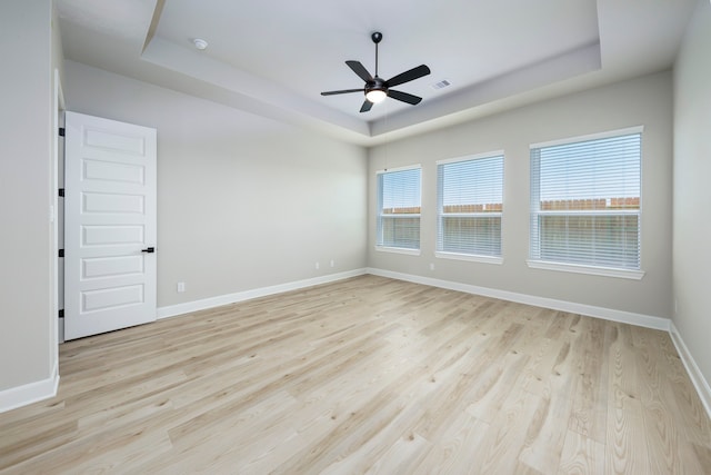 empty room with light wood finished floors, baseboards, visible vents, ceiling fan, and a raised ceiling