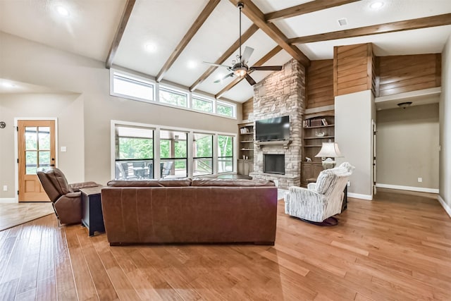 living area featuring beam ceiling, baseboards, a stone fireplace, ceiling fan, and light wood-type flooring