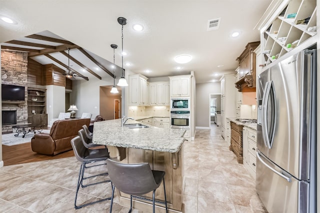 kitchen with visible vents, open floor plan, light stone counters, a sink, and appliances with stainless steel finishes