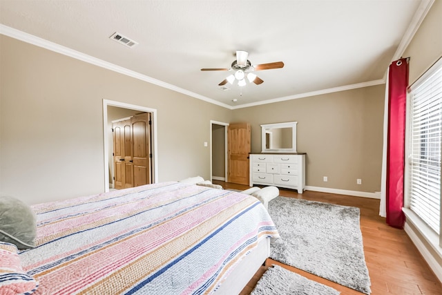 bedroom featuring light wood-style flooring, a ceiling fan, baseboards, visible vents, and ornamental molding