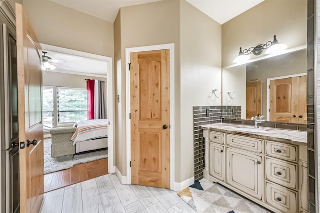 bathroom featuring a ceiling fan, wood finished floors, vanity, baseboards, and ensuite bath