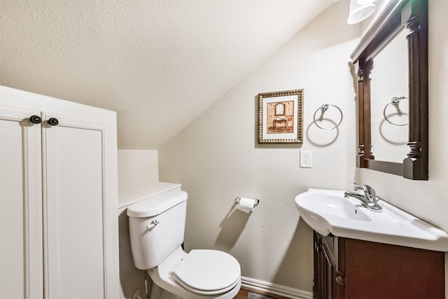 half bathroom with a textured ceiling, vaulted ceiling, vanity, baseboards, and toilet