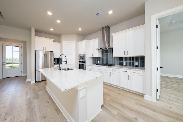 kitchen with wall chimney exhaust hood, stainless steel appliances, a kitchen island with sink, a sink, and visible vents