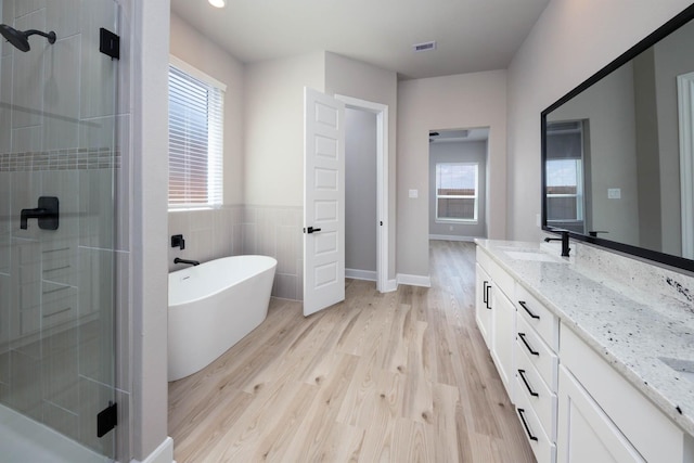 full bathroom featuring a wealth of natural light, vanity, wood finished floors, and a stall shower